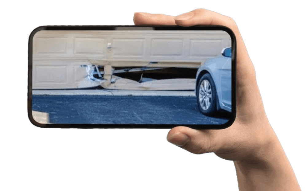 A hand holding a smartphone photographing a damaged garage door panel to share with Maverick