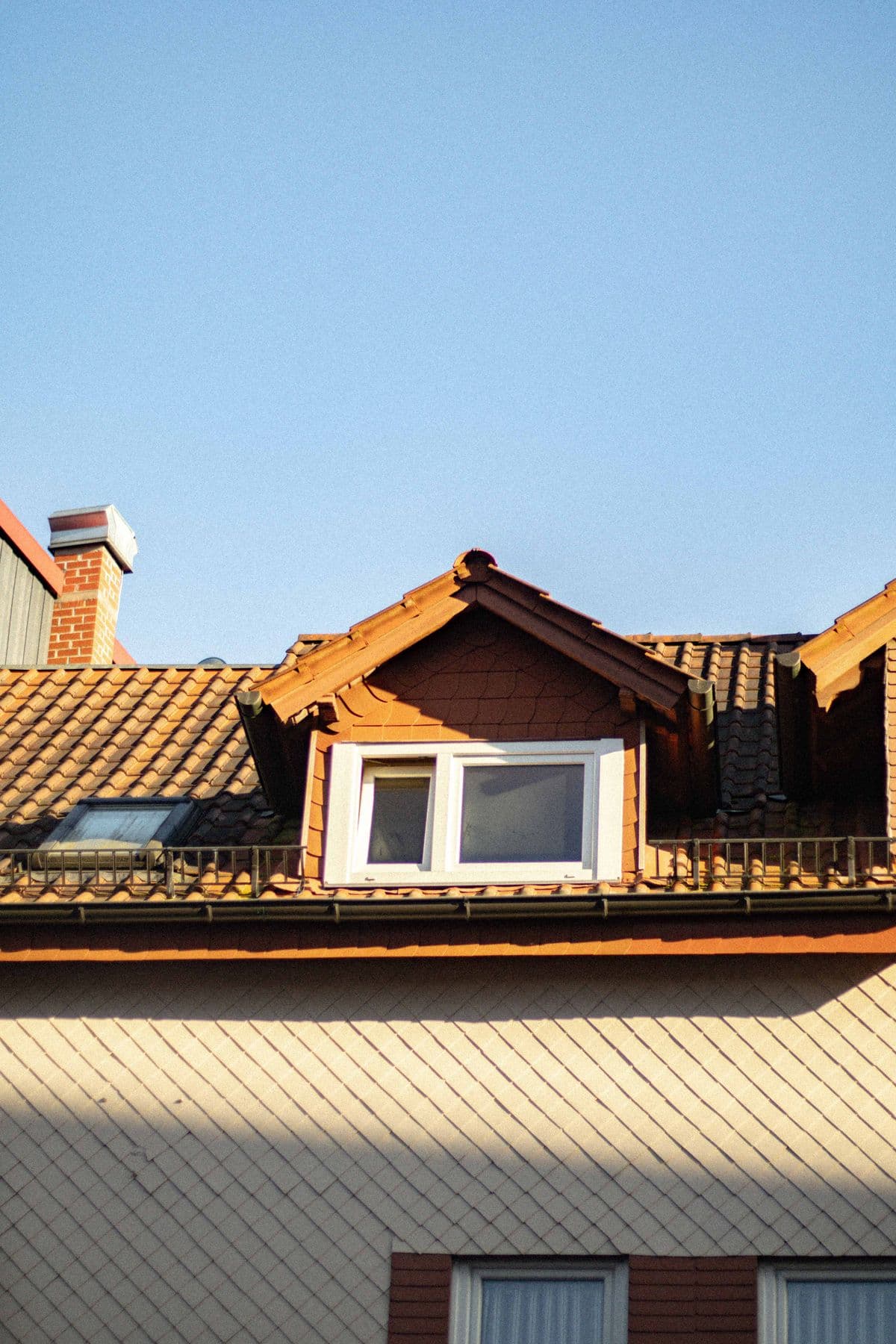 Warm terracotta roof with a dormer window against a clear blue sky