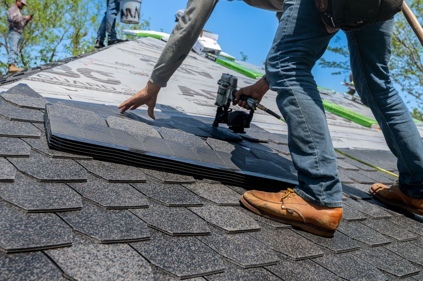 Roofer using a nail gun to install asphalt shingles on a new roof